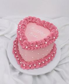 a heart shaped cake on a white plate with pink icing and pearls around the edges