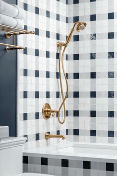 a bathroom with black and white tiles on the walls, gold fixtures and a bathtub