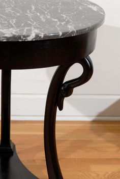 a marble top table with black legs on wooden flooring and white walls in background