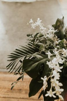 a vase filled with white flowers and greenery on top of a wooden table next to a wall