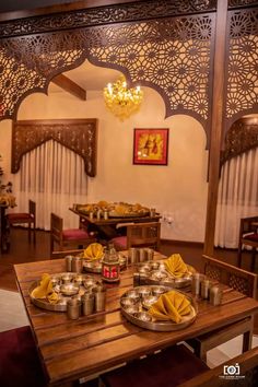 a wooden table topped with metal pans covered in food next to a chandelier