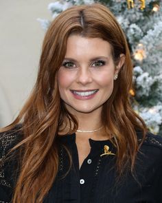 a woman with long red hair smiles for the camera while standing in front of a christmas tree