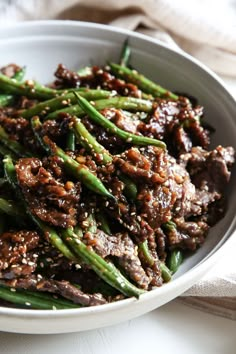 a white bowl filled with meat and asparagus