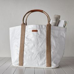 Market tote, gym bag, everyday carryall—this dynamo goes by all of the above. It’s fashioned from Uashmama’s signature washable paper and topped off with a water-resistant, glossy finish. (That means it’ll wipe down in a flash.) Shoutout to the inner pocket, magnetic closure, and cotton handles that give it extra versatility. AGGO® washable paper exterior. Cotton interior. Handles made of 85% recycled t-shirts. Water-resistant glossy finish. Generously sized, yet lightweight. Magnetic snap closu White Canvas Bag With Top Carry Handle For Everyday, Functional White Shoulder Bag With Top Carry Handle, White Large Capacity Travel Bag For Everyday, Practical White Tote Bag, Practical White Bag For Daily Use, Practical White Shoulder Bag For Everyday Use, Functional White Canvas Bag For On-the-go, White Canvas Bag With Reinforced Handles, Practical White Bags For Everyday Use