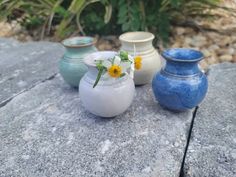 three vases sitting on top of a rock next to each other with flowers in them