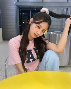 a woman sitting on the ground with her hair in a ponytail and wearing a pink shirt