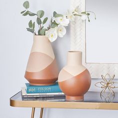 two vases with flowers are sitting on a shelf next to a mirror and books