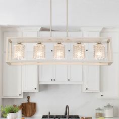 a kitchen with white cabinets and an island light fixture over the stove top, surrounded by wooden utensils