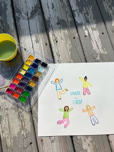 a child's drawing with paint and watercolors on a wooden table next to a cup