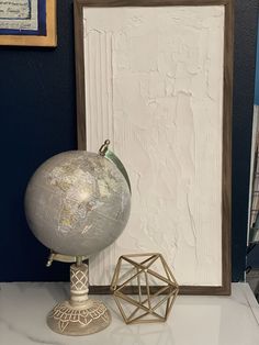 a small globe sits on a table next to an ornament and framed artwork