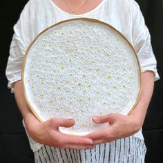 a woman holding a white and yellow plate with daisies on it in her hands