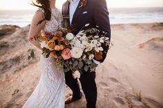 a bride and groom standing on the beach with their bouquets in front of them