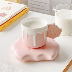 a pink and white cup sitting on top of a table next to a glass of milk