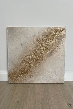 a silver and gold painting sitting on top of a wooden floor next to a white wall