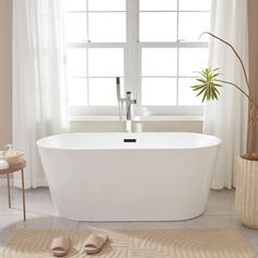 a white bath tub sitting in front of a window next to a potted plant