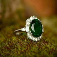 an emerald and diamond ring sits on moss