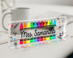 a white mug sitting on top of a desk next to a sign with crayons