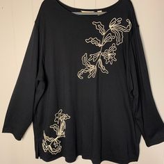 a black shirt with gold embroidered flowers on the front and back, hanging from a hanger