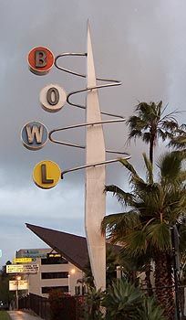 a street sign on the side of a road with palm trees and buildings in the background