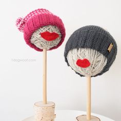 two knitted hats sitting on top of wooden sticks in front of a white wall