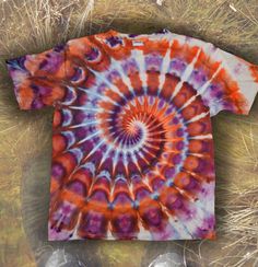 an orange, purple and blue tie - dyed t - shirt laying on top of dry grass