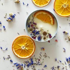 orange slices and dried flowers in a bowl on a white surface with petals scattered around them