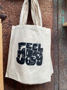 a tote bag hanging on the side of a building with words feel more joy printed on it