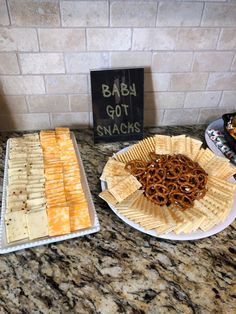 two trays filled with crackers and pretzels next to a sign that says baby got snacks