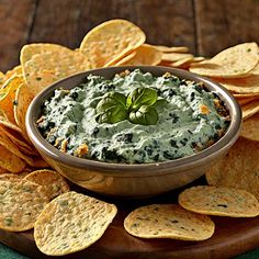 a bowl of dip surrounded by tortilla chips on a wooden platter with a green leaf in the center