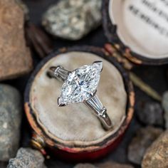 an engagement ring sitting on top of a wooden box surrounded by rocks and stones,