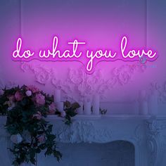 a pink neon sign that says do what you love with candles and flowers in front of it