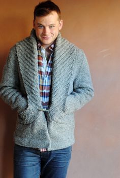 a man standing in front of a brown wall wearing a sweater and jeans with his hands in his pockets