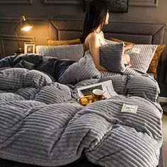 a woman sitting on a bed with grey comforter and pillows