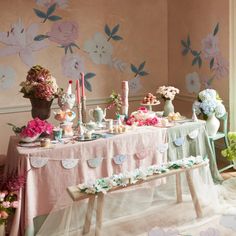 a table with flowers and candles on it in front of a wallpapered room