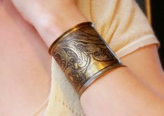 a woman's arm wearing a gold bracelet with intricate designs on the wrist and in the other hand