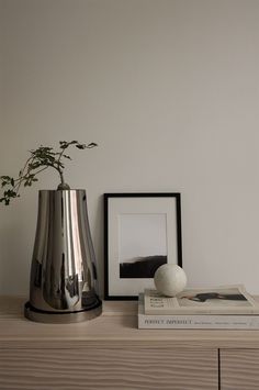 a silver vase sitting on top of a wooden table next to books and a plant