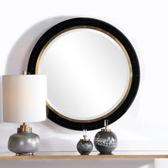 a round mirror sitting on top of a table next to two vases and a lamp