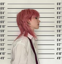 a woman with pink hair is standing in front of a mugshot wall and wearing a tie