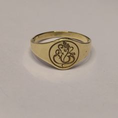 a gold ring with an image of ganeshi on the front and side, sitting on a white surface