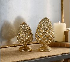 two gold pinecone candlesticks sitting on a table next to a mirror