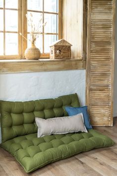 a green futon couch sitting in front of a window with two pillows on it