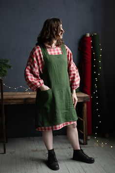 a woman standing in front of a christmas tree wearing an apron dress and black boots