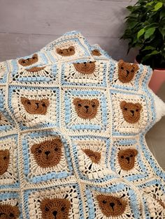 a crocheted blanket with bears on it sitting next to a potted plant