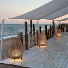 an outdoor seating area on the beach with lights and umbrellas set up to look out onto the ocean