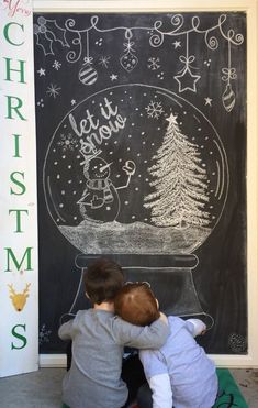 two children are sitting in front of a chalkboard with a christmas scene on it