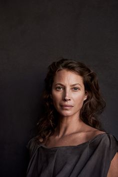 a woman wearing a black dress and posing for a photo in front of a dark background