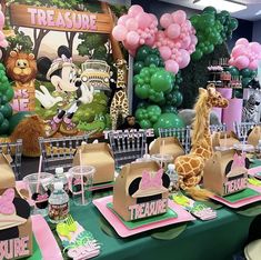 a table set up with pink and green balloons, giraffes, and other decorations