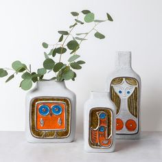 three ceramic vases sitting next to each other on a table with a plant in it