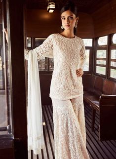 a woman standing on a wooden floor wearing a white dress with long sleeves and lace detailing