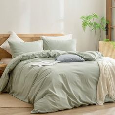 an unmade bed with green sheets and pillows on the floor next to a window